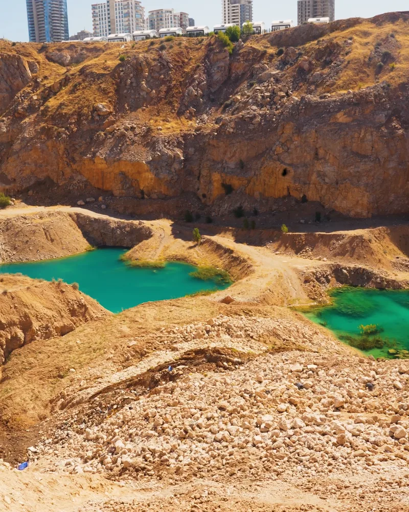A quarry with turquoise ponds against the city skyline.